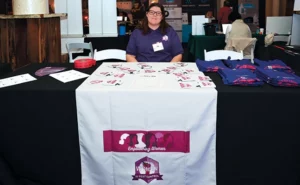 The 2025 Women in Pest Control conference took place March 6–7 in Kansas City, Mo. Staffer McKenzie Futrell sits behind the official WIPC table with a variety of bags, T-shirts, drink cozies, stickers and more for attendees. PHOTO: WIPC